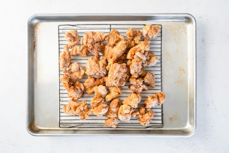 general tsos chicken pieces after frying on a wire rack set in a baking sheet.