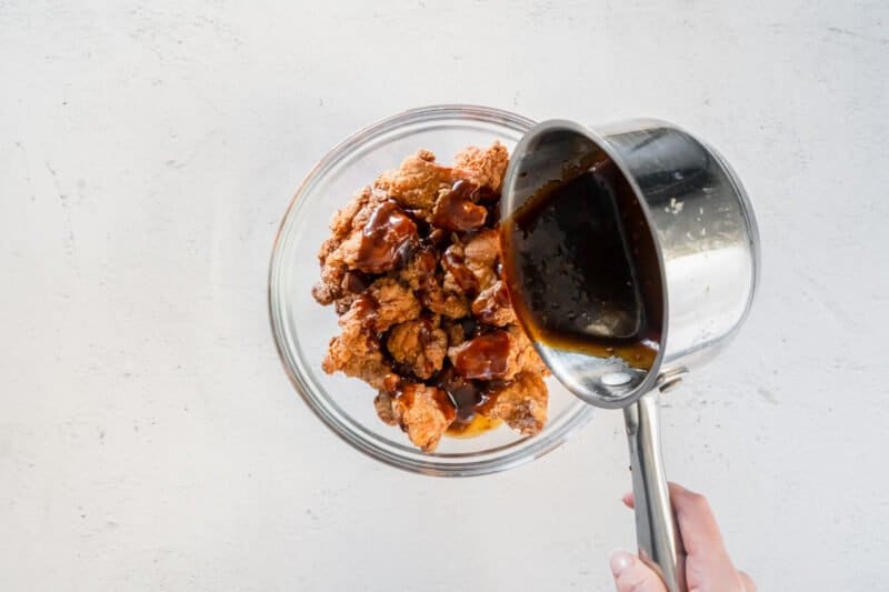 general tsos sauce poured over fried chicken bites in a glass bowl.