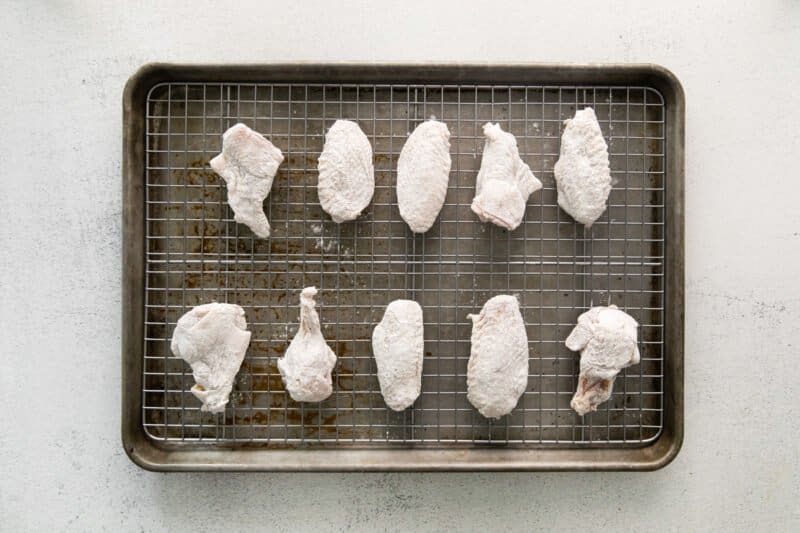 10 flour coated chicken wings on a wire rack set in a baking sheet.