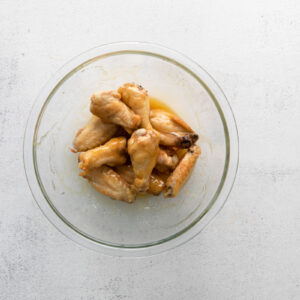 hot honey chicken wings tossed in hot honey sauce in a glass bowl.