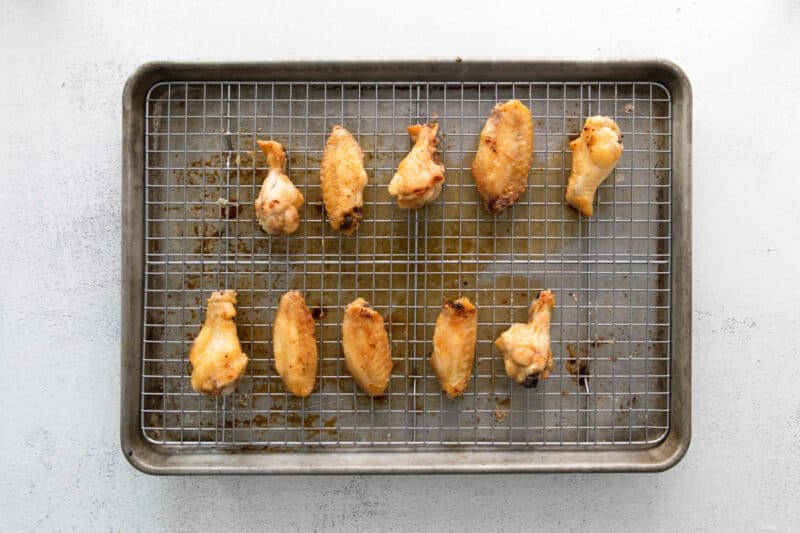 10 broiled hot honey chicken wings on a wire rack set in a baking sheet.