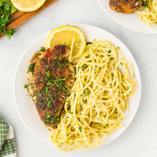 overhead view of lemon pepper chicken with pasta on a white plate.