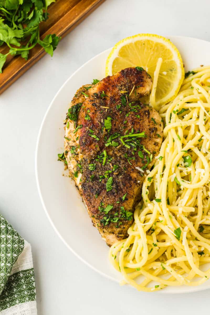 overhead view of lemon pepper chicken with pasta on a white plate.