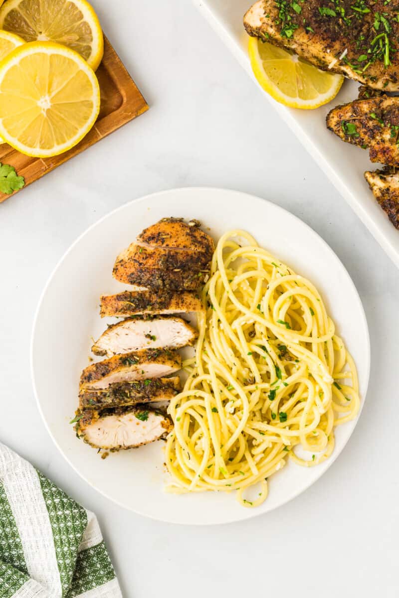 sliced lemon pepper chicken breast with pasta on a white plate.
