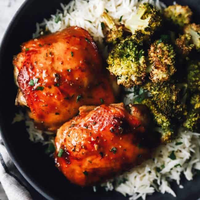 sheet pan chicken and broccoli over rice in a black bowl.