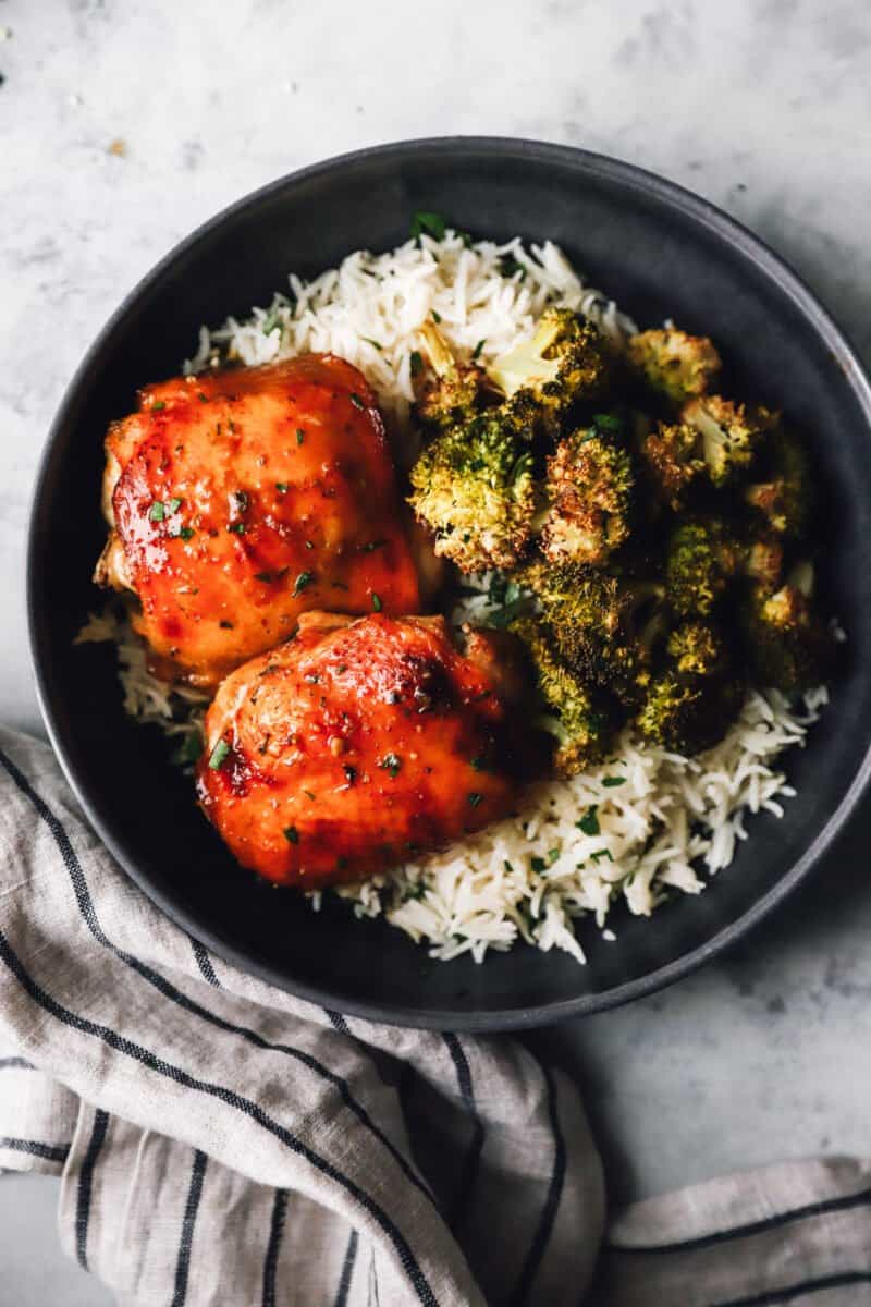 sheet pan chicken and broccoli over rice in a black bowl.