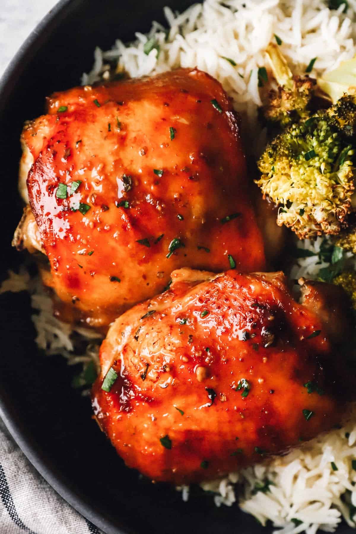 close up of sheet pan chicken and broccoli over rice in a black bowl.