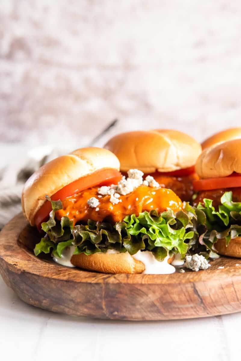 3 fried buffalo chicken sandwiches on a wooden serving tray.