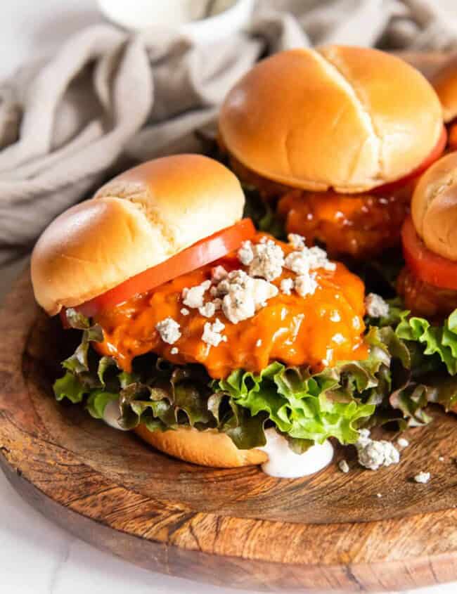 3 fried buffalo chicken sandwiches on a wooden serving tray.