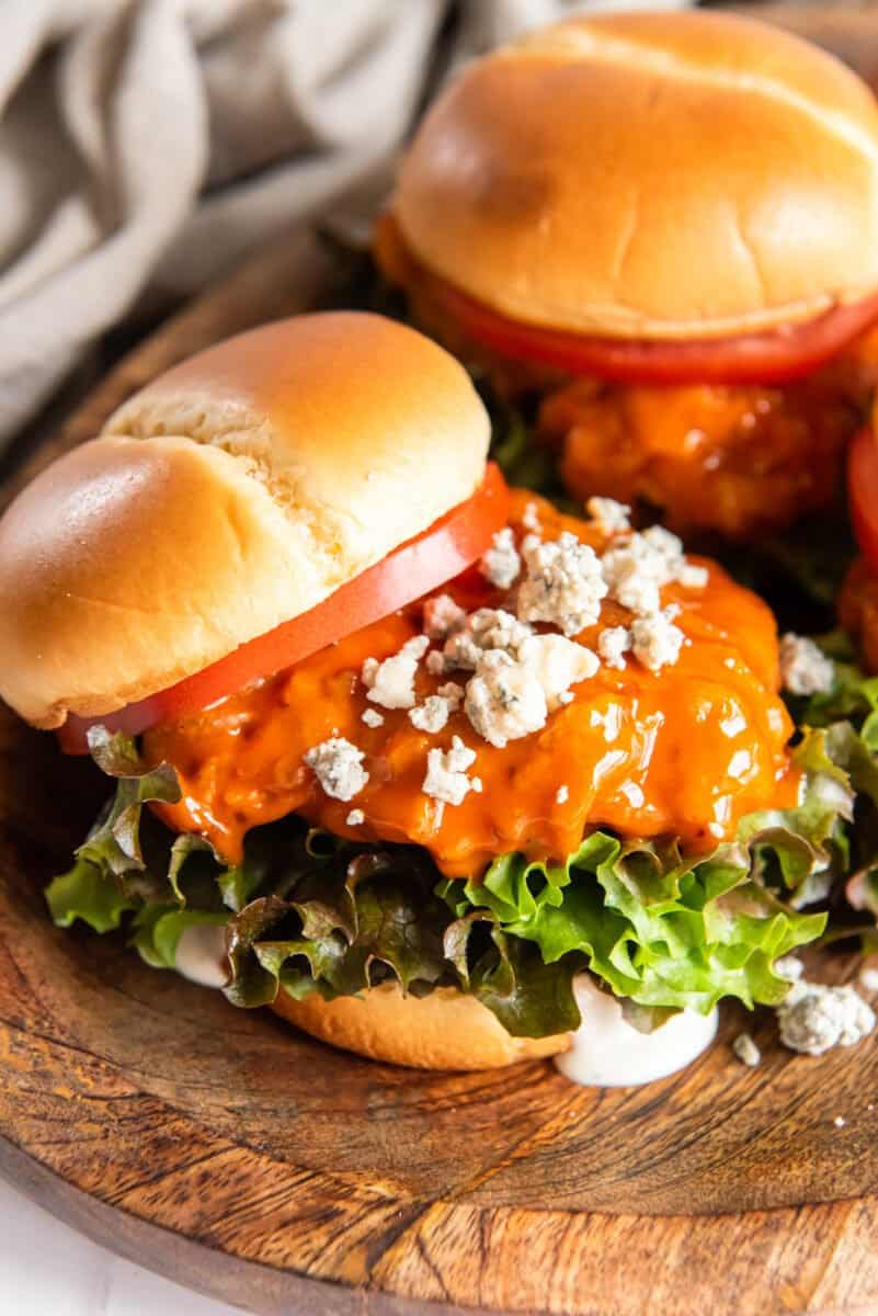 close up of fried buffalo chicken sandwiches on a wooden serving tray.