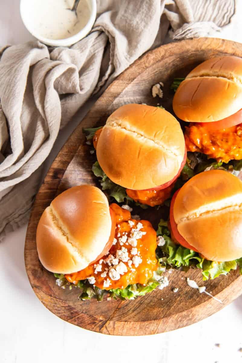 overhead view of 4 fried buffalo chicken sandwiches on a wooden serving tray.