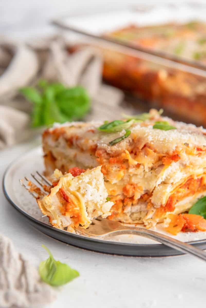 a forkful of chicken parmesan lasagna next to a slice on a white plate.