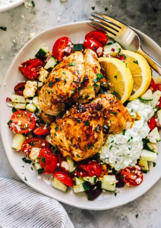 a plate of greek chicken thighs on a bed of greek salad