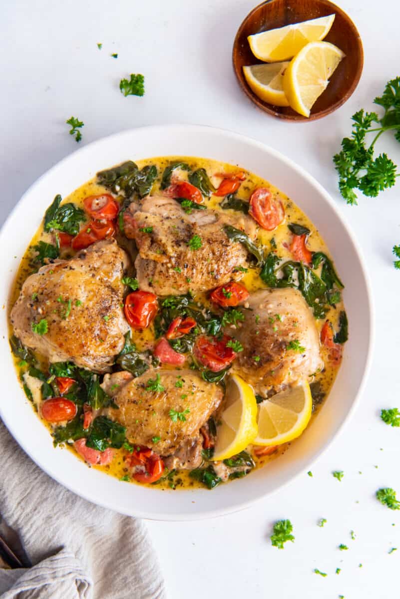 instant pot tuscan chicken with lemon wedges in a large white serving bowl.