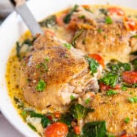 instant pot tuscan chicken in a large white serving bowl with a serving spoon.