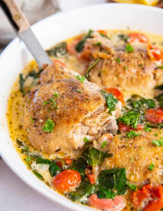 instant pot tuscan chicken in a large white serving bowl with a serving spoon.