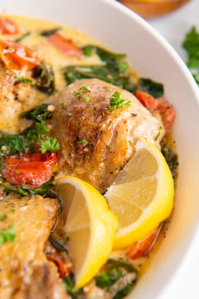 close up of instant pot tuscan chicken with lemon wedges in a large white serving bowl.