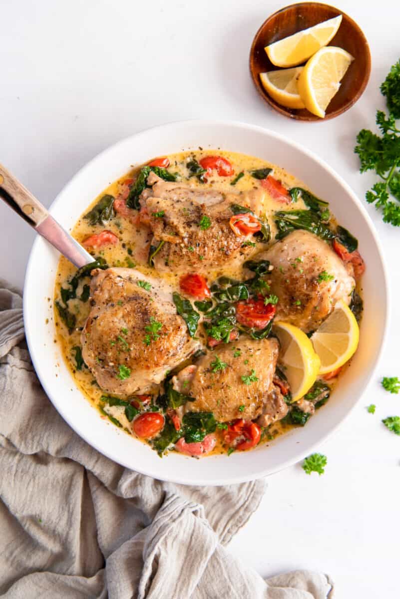 instant pot tuscan chicken in a large white serving bowl with a spoon.