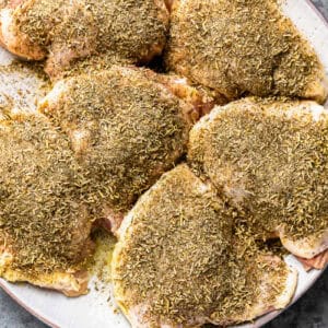 seasoned raw chicken thighs on a white plate.