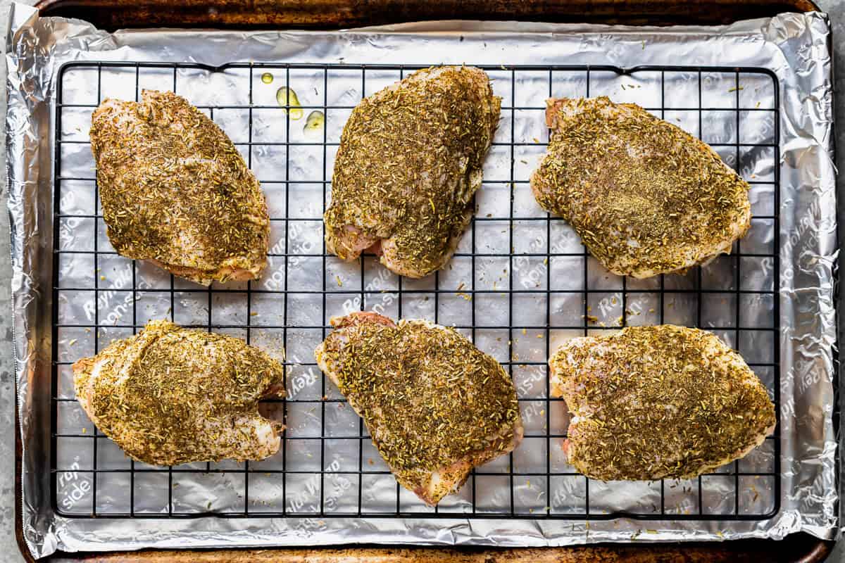 seasoned raw chicken thighs on a wire rack set in a baking sheet.