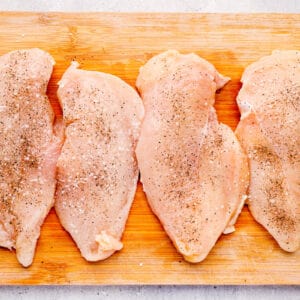 2 chicken breasts sliced in half on a wood cutting board.