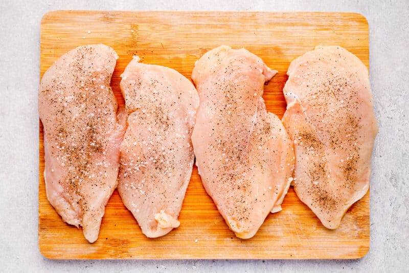 2 chicken breasts sliced in half on a wood cutting board.