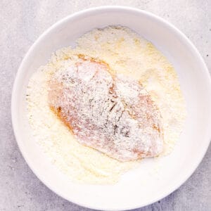 chicken breast dredged in flour in a white bowl.
