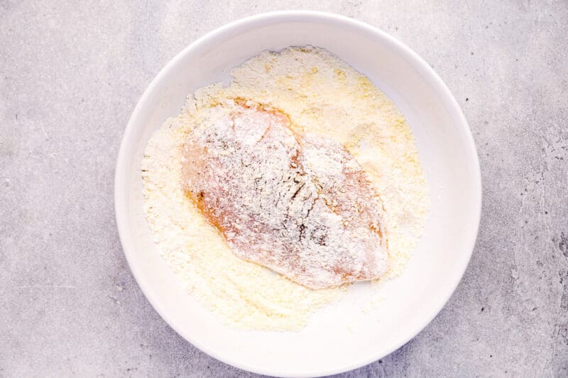 chicken breast dredged in flour in a white bowl.