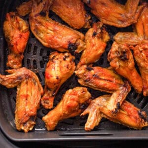cooked chicken wing portions in an air fryer basket.