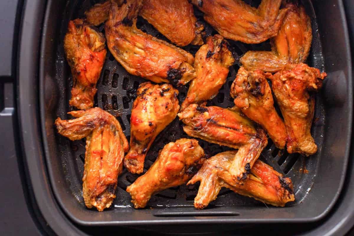 cooked chicken wing portions in an air fryer basket.
