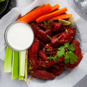 air fryer hot honey chicken wings on a parchment-lined serving platter with carrot and celery sticks and blue cheese dressing.
