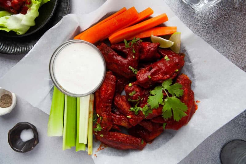 air fryer hot honey chicken wings on a parchment-lined serving platter with carrot and celery sticks and blue cheese dressing.
