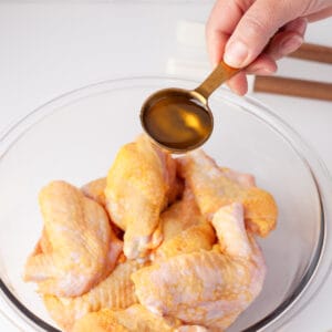 olive oil poured over chicken wings in a glass bowl.