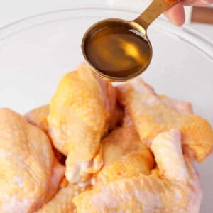 pouring oil over raw chicken wing portions in a glass bowl.