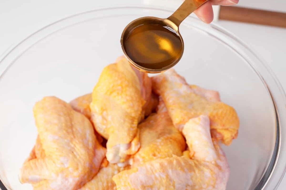 pouring oil over raw chicken wing portions in a glass bowl.