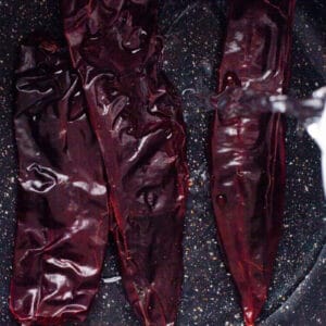 pouring water over dried guajillo chiles in a pan.