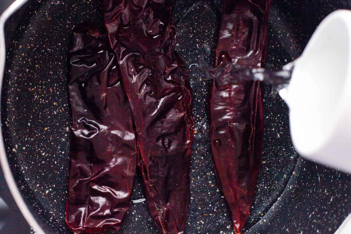 pouring water over dried guajillo chiles in a pan.