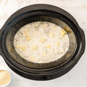 butter scattered over crockpot chicken alfredo in a crockpot.