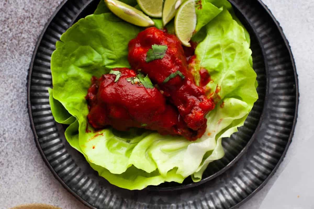 two air fryer hot honey chicken wings on a lettuce leaf on a plate with lime wedges and cilantro.