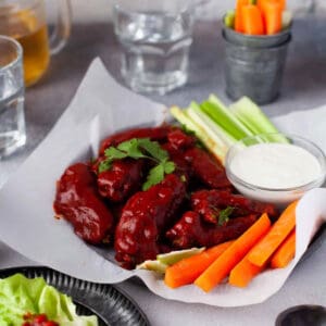 air fryer hot honey chicken wings on a parchment lined plate with carrot and celery sticks and blue cheese dressing.