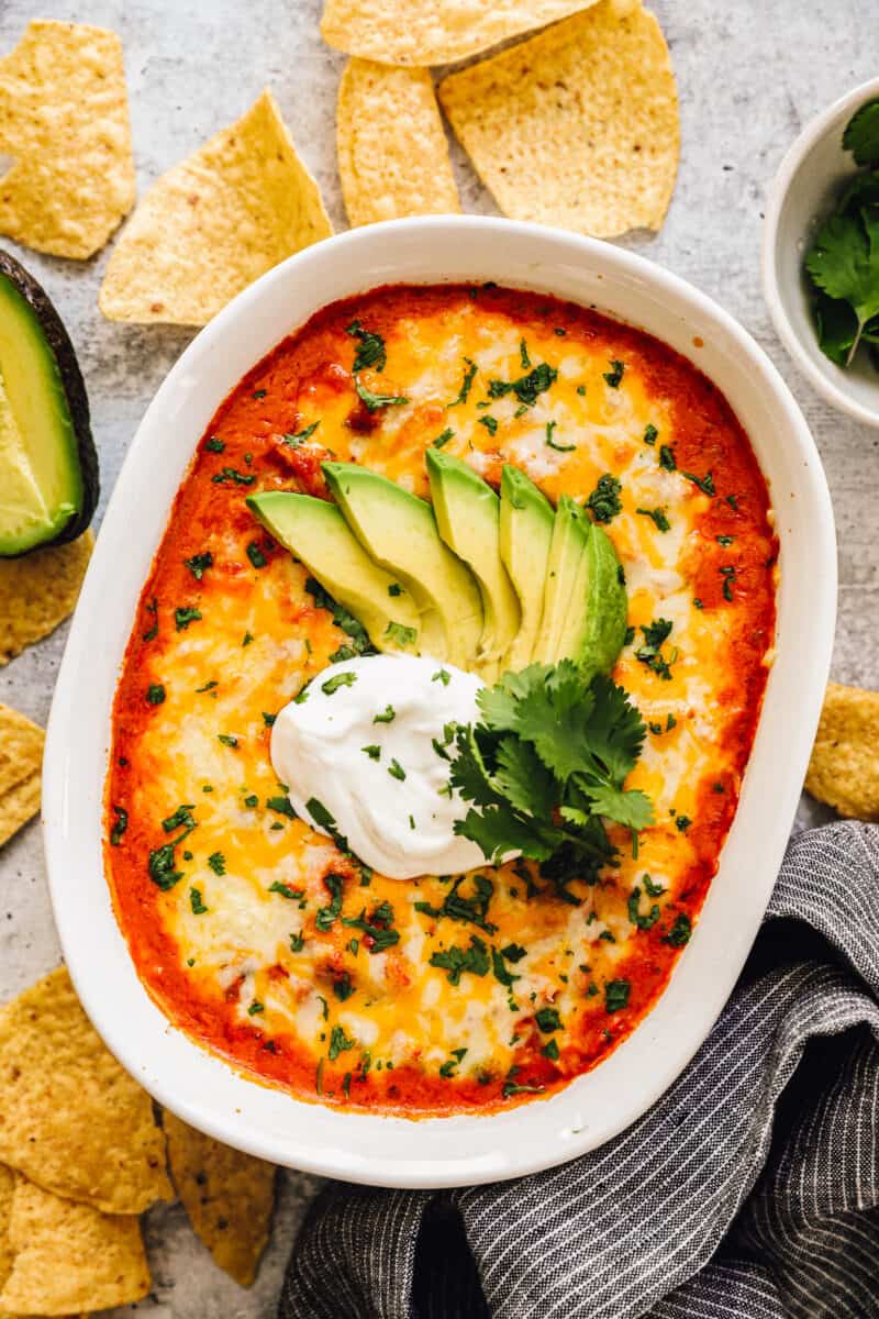 baked chicken enchilada dip topped with avocado slices and sour cream