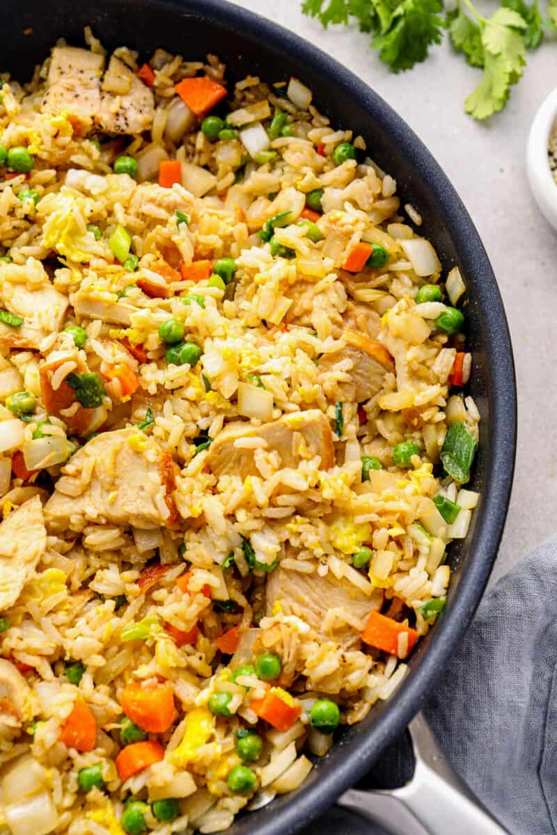 a skillet of fried rice with chicken, peas, and carrots