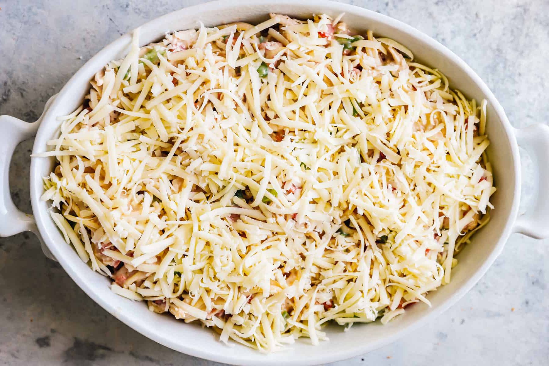 chicken spaghetti casserole before baking, topped with unmelted cheese