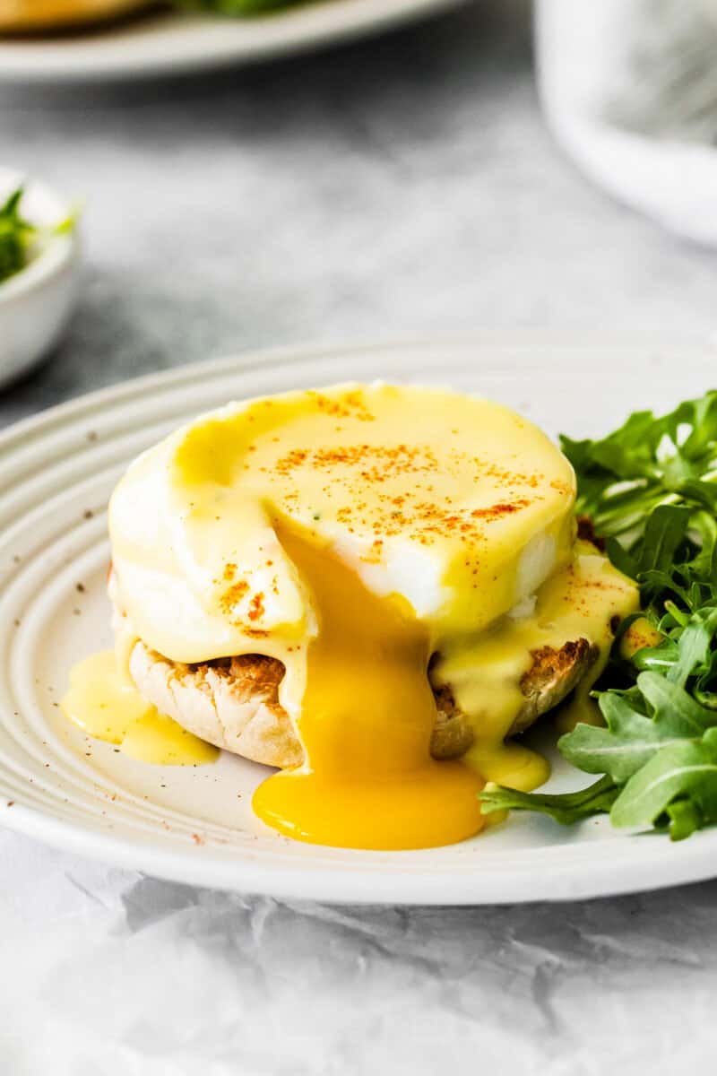 cut eggs benedict on a white plate with arugula.