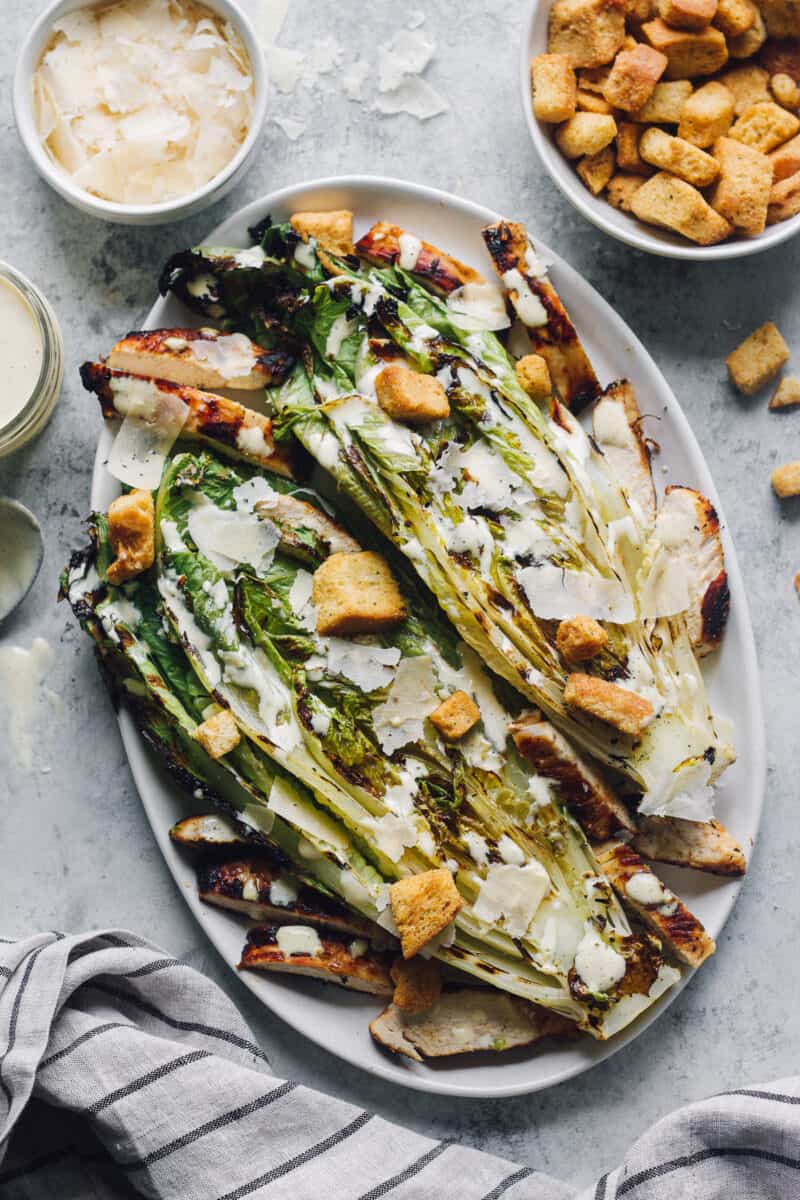 plate of grilled chicken caesar salad surrounded by bowls of ingredients