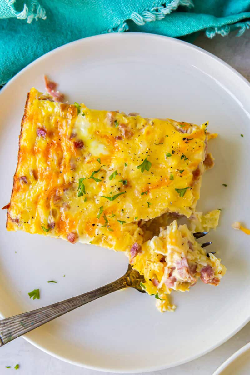 a forkful of ham and cheese breakfast casserole on a white plate.
