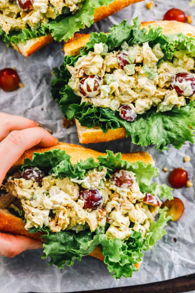 three chicken salad sandwiches laying on a table, with a hand grabbing one of them
