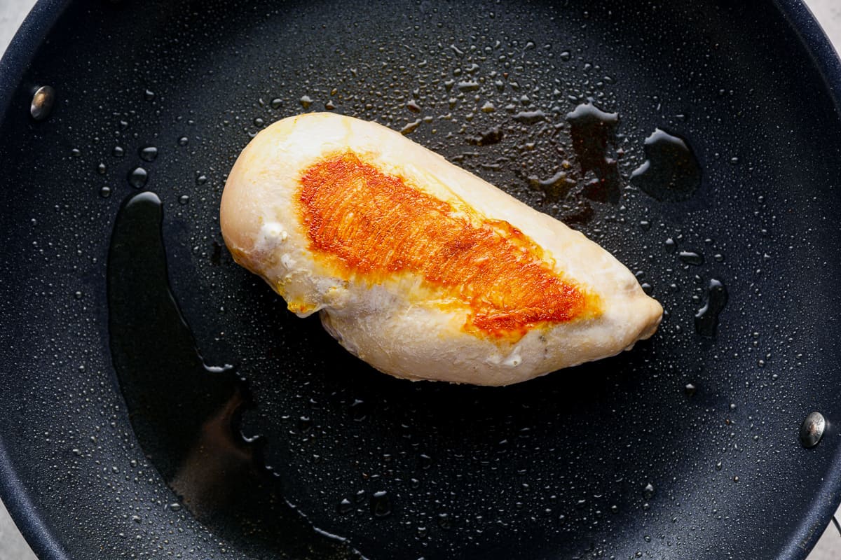 Browned chicken breast cooking in a skillet.