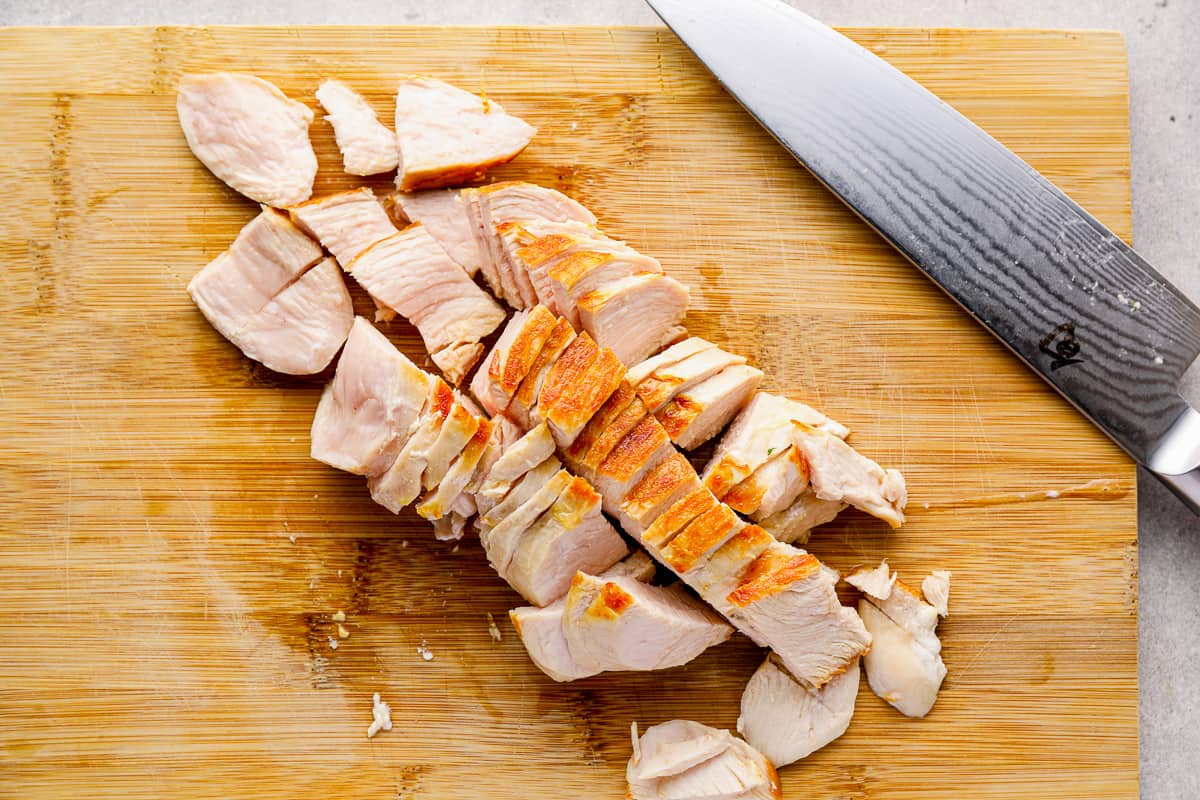 Chicken breast on a cutting board with a Chef's knife, cut into small pieces.