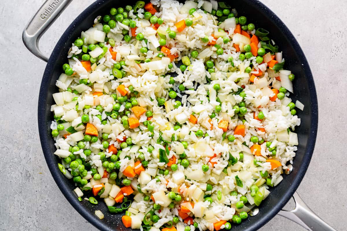 White rice, peas, carrots, and onions cooking in a skillet.